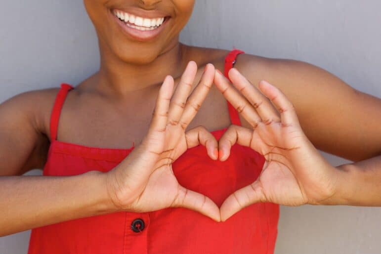Close up portrait of young woman smiling with heart shape hand