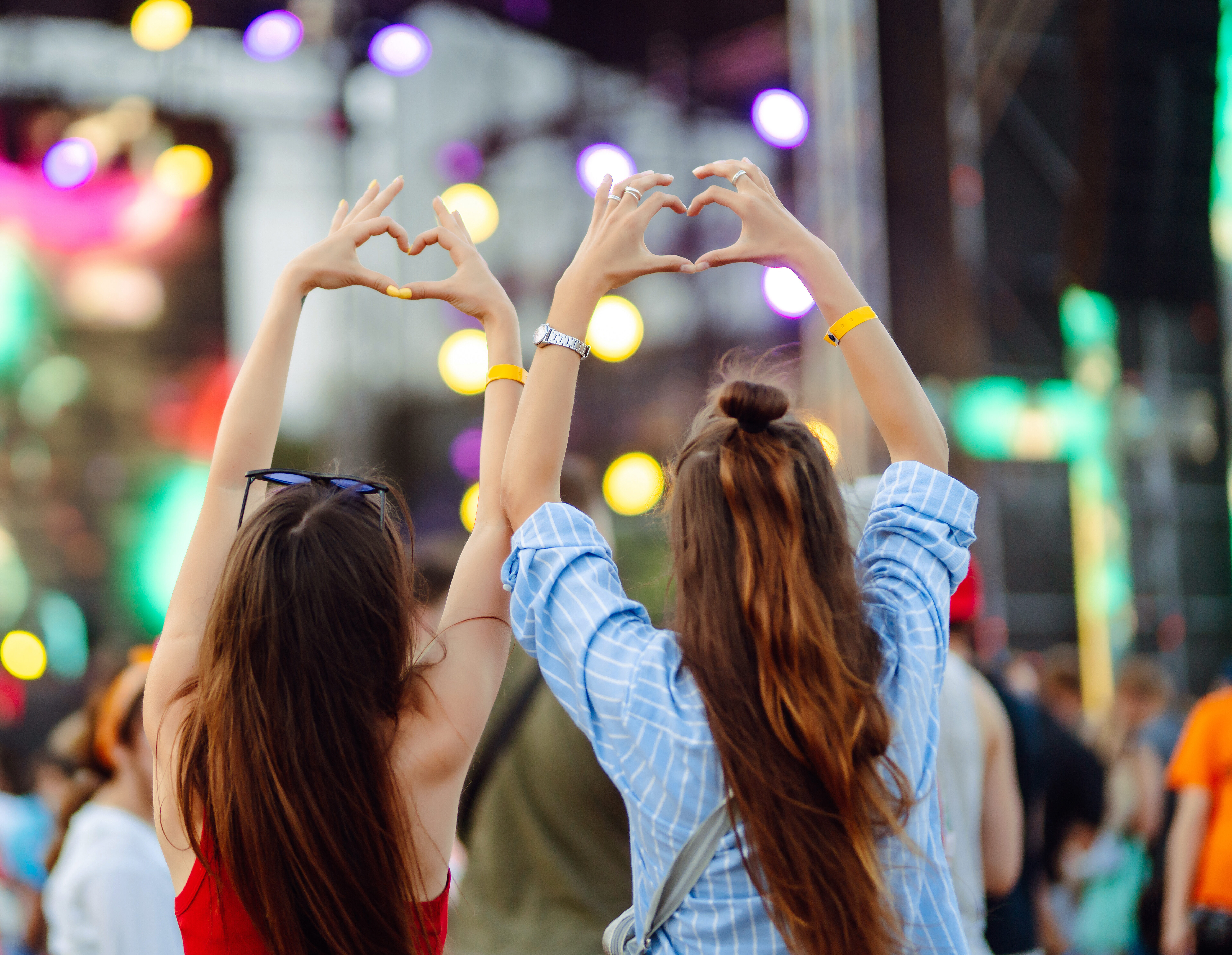 heart shaped hands at concert, loving the artist and the festival. music concert with lights and silhouette of people enjoying the concert.